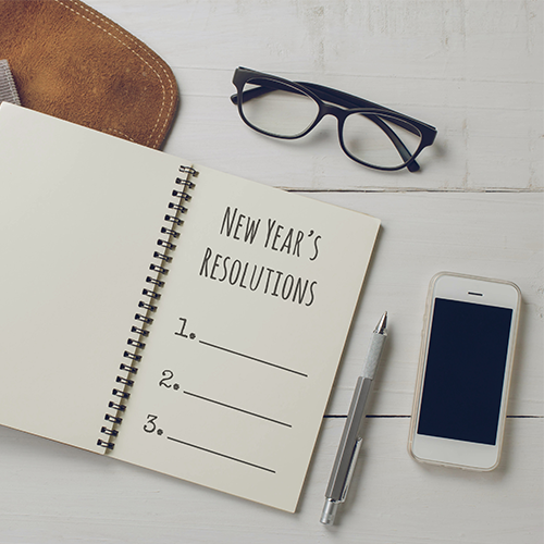 notebook with new year's resolutions on table with glasses pen and phone