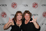 Two individuals signing stand in front of a white CSUN background