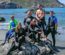 A group of marine biology students in scuba gear on the beach.